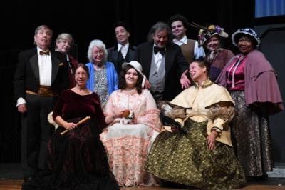 Cast members gather on stage in costume with director.