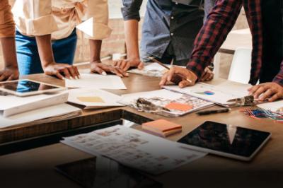 A group of people work at a table with charts, graphs, and paperwork.