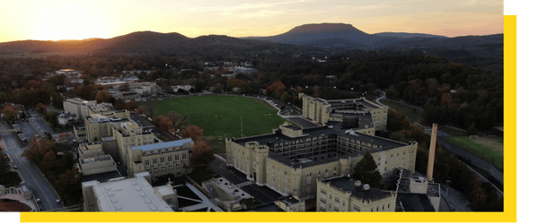 Aerial view of post - VMI's campus - with the sun setting over the mountains in the background.