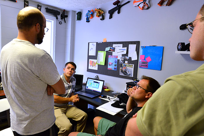 Three men and a student sit in a room