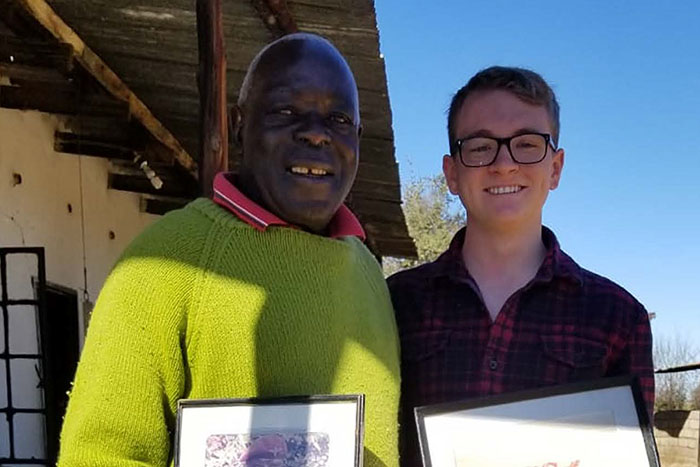 A students stands with a Zimbabwean man holding two certificates