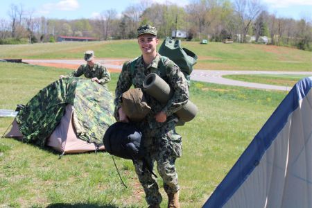 NROTC cadet stands near tents used during spring field training exercises.