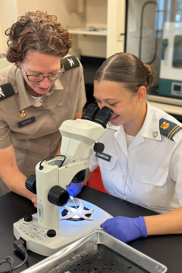 A professor and student (cadet) in the Department of Biology use a microscope during a lab session.