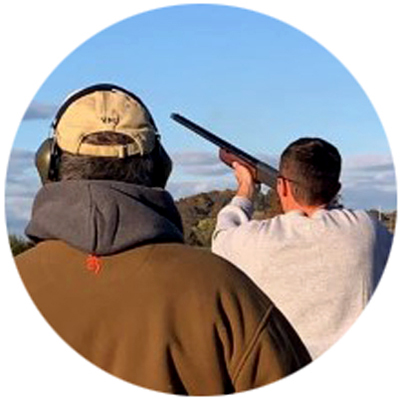 Trap and Skeet Club cadet member raising shotgun toward sky with professional member watching photo circle