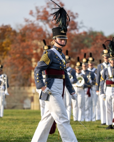 A cadet leader marches in parade, facing the audience during review.
