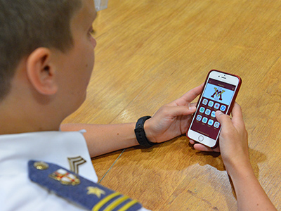 A cadet holds a cell phone displaying the Reach Out app.