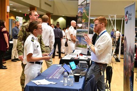 A female cadet talks with a representative from the Peace Corps during a career fair