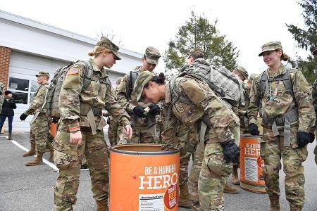 Cadets put canned food into a large orange barrel.