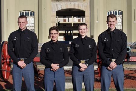 Four cadets who received direct commissions into the U.S. Coast Guard through VMI, a military college, pose in front of barracks.