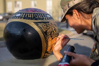 A female student (cadet) at VMI paints this year's ring design onto a cannonball.