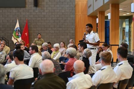 Cadet standing holding a microphone and addressing a large gathering of VMI cadets, faculty, staff, and the general public