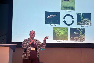 Lt. Col. Molly Kent discusses her research in front of life cycle slide.