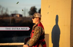 A cadet stands outside a shooting course with bullet shells flying.