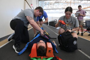 Cadets strap their peer to a spine board to immobilize him before transport during a scenario-based drill in the Corps Physical Training Facility.