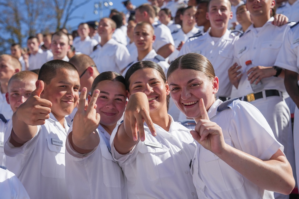 Cadets enjoy the game from the stands, forming V-M-I with their hands.