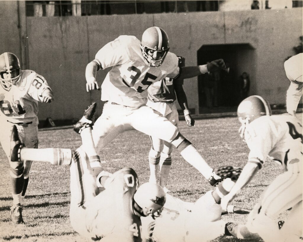  VMI vs VPI football game, football player jumps over other players on the field.